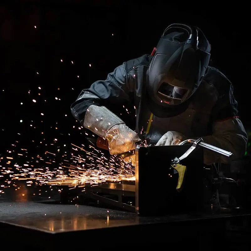 Welder using CleanAIR Verus Air Welding Helmet with sparks flying in a dark workshop.